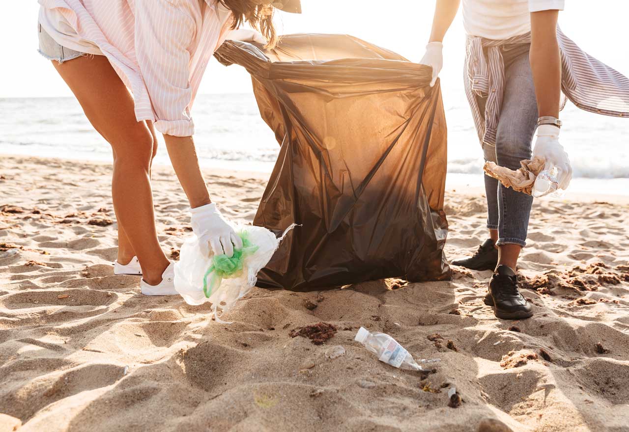 Zwei Personen sammeln Plastikmüll am Meer auf.