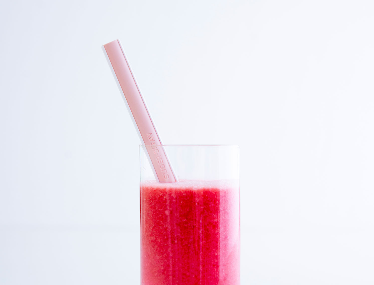 Ein rosafarbener Sliderstraw Mehrweg-Strohhalm liegt in einem Glas mit rotem Smoothie.